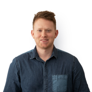 A young man wearing a denim style smart shirt, with short ginger hair and facial stubble